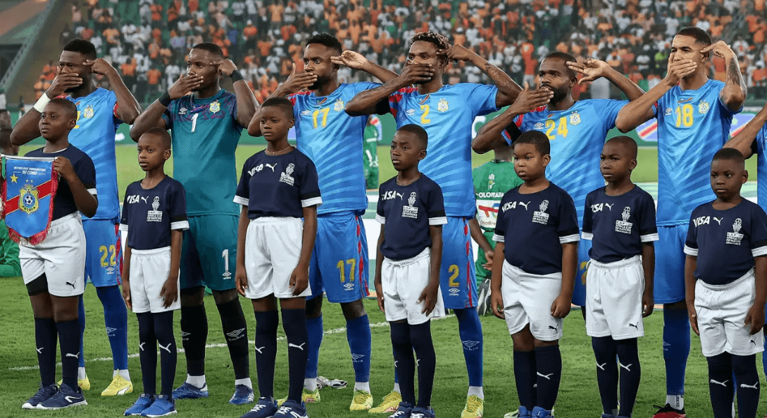 Congolese football players hold one hand to their head like a gun and one hand over their mouth